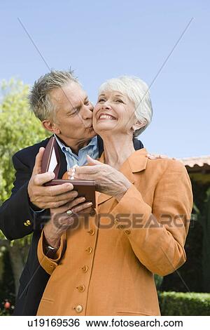 Stock Photograph - Senior man kissing wife on cheek and giving present. Fotosearch