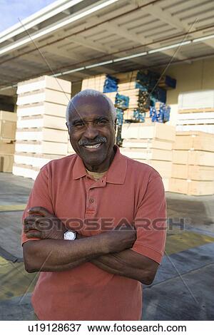 Stock Photo - Senior man outside warehouse full of wood. Fotosearch