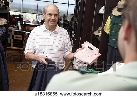 Stock Photography - Senior Man standing in Golf Shop, asking clerk about shirt. Fotosearch