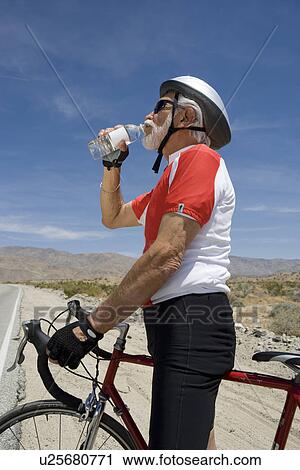 Stock Image - Senior man with bike drinking water. Fotosearch