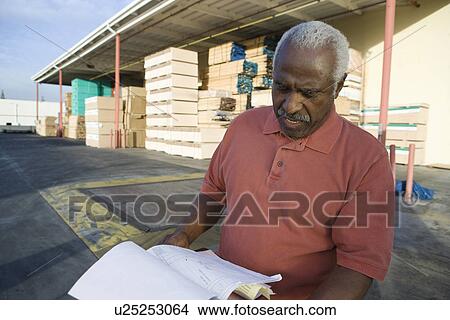 Picture - Senior man with clipboard outside warehouse full of wood. Fotosearch