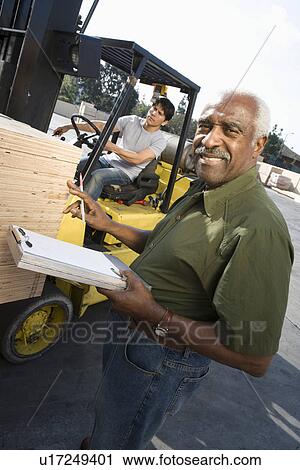 Stock Image - Senior warehouseman and mid-adult forklift truck driver. Fotosearch