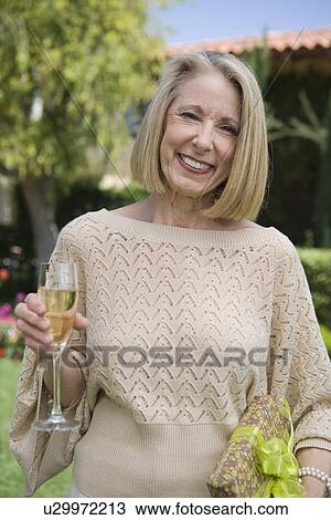 Senior woman holding present and glass of champagne View Large Photo Image Stock Image - Senior woman holding present and glass of champagne. Fotosearch