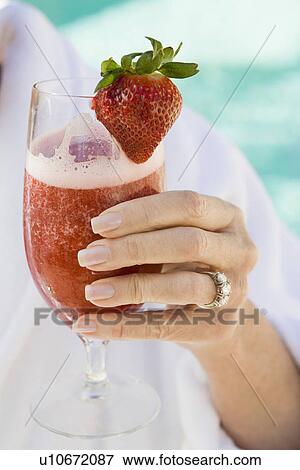 Stock Photo - Senior woman holding strawberry cocktail, close-up. Fotosearch