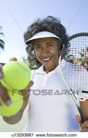 Stock Photo - Senior woman holding tennis racket and balls, portrait. Fotosearch
