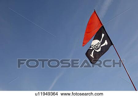 Picture - Skull and crossbones flag and red flag against blue sky. Fotosearch
