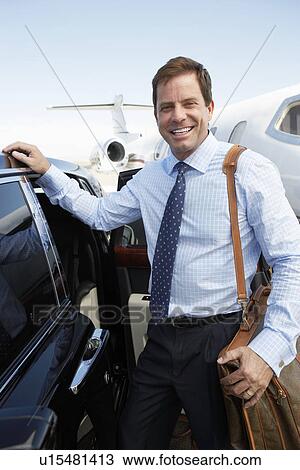 Stock Image - Smiling businessman standing beside car near private jet before Leaving on Business Trip. Fotosearch