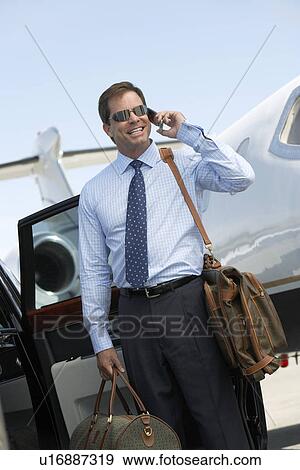 Smiling businessman standing beside car near private jet, talking on mobile before Leaving on Business Trip View Large Photo Image Stock Photo - Smiling businessman standing beside car near private jet, talking on mobile before Leaving on Business Trip. Fotosearch