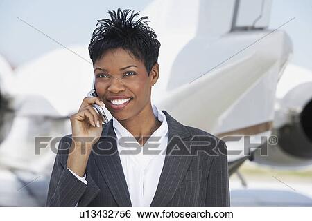 Smiling Businesswoman standing outside Airplane, talking on mobile View Large Photo Image Stock Photograph - Smiling Businesswoman standing outside Airplane, talking on mobile. Fotosearch