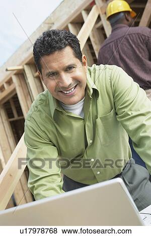 Stock Photo - Smiling Construction Worker Using Laptop on construction Site. Fotosearch