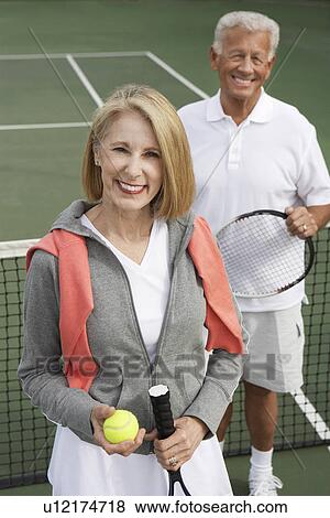 Stock Photo - Smiling Couple standing on Tennis Court, holding rackets and ball. Fotosearch