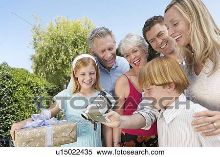 Stock Photography - Smiling Family standing outside, Filming a Celebration. Fotosearch
