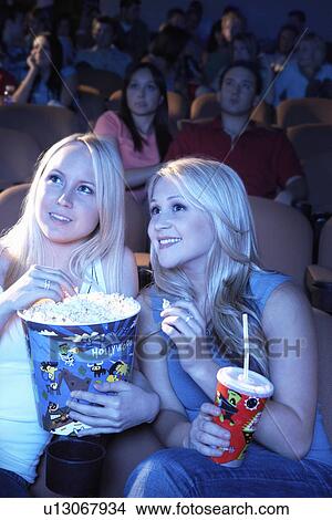 Picture - Smiling Friends sitting in theatre with popcorn and soda, Watching Movie. Fotosearch