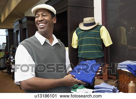 Stock Image - Smiling Man wearing golf apparel in Golf Shop holding shirt near manikin. Fotosearch