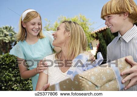 Stock Photograph - Smiling mother receiving gift from children outside. Fotosearch