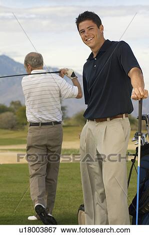 Stock Photo - Smiling Young Man standing on Golf Course with Older man. Fotosearch