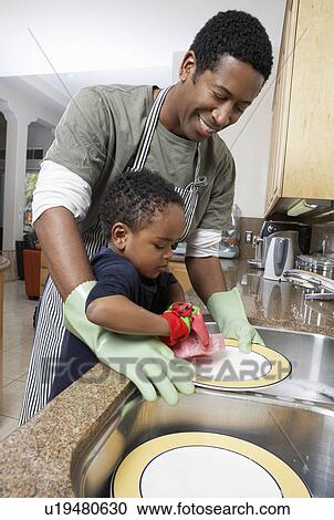 Stock Image - Son (3-6) helping father wash dishes. Fotosearch