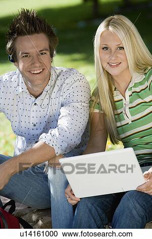 Stock Image - Student couple relaxing outdoors, (portrait). Fotosearch
