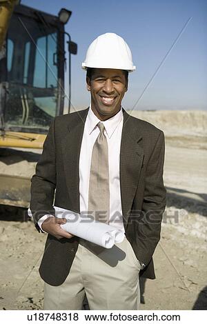 Stock Photo - Surveyor holding blueprints on construction site, portrait. Fotosearch