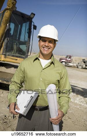 Stock Photograph - Surveyor holding blueprints on construction site, portrait. Fotosearch