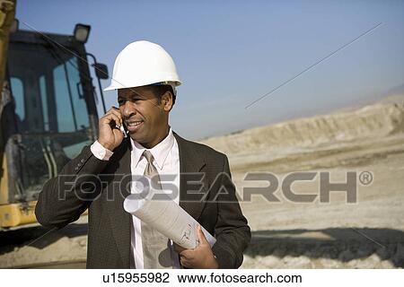 Stock Image - Surveyor using mobile phone on construction site. Fotosearch