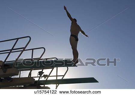 Stock Image - Swimmer standing on diving board at sunset. Fotosearch