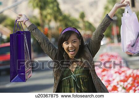 Stock Photography - Teenage girl (16-17) raising shopping bags in street, (portrait). Fotosearch