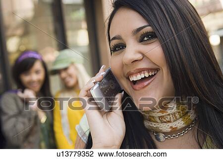 Stock Image - Teenage girl (16-17) using mobile phone, laughing, outdoors. Fotosearch