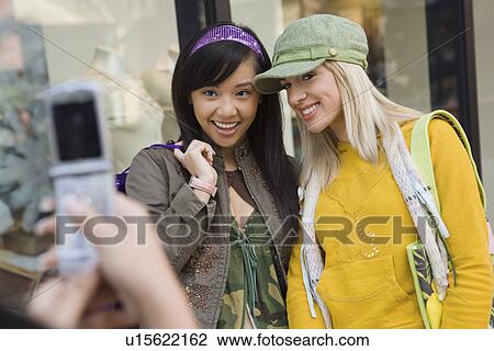 Stock Image - Teenage girl photographing friends using camera phone, outdoors. Fotosearch