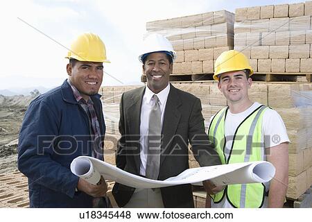 Stock Photo - Three construction workers standing on construction site with blueprints. Fotosearch