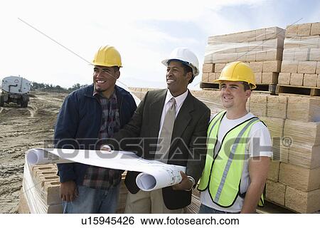 Three construction workers standing on construction site with blueprints View Large Photo Image Stock Photograph - Three construction workers standing on construction site with blueprints. Fotosearch