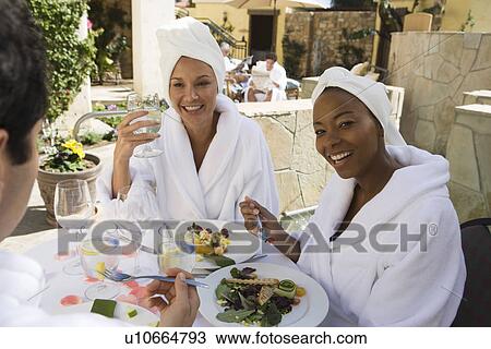 Stock Image - Three friends in bathrobes, eating outdoors. Fotosearch
