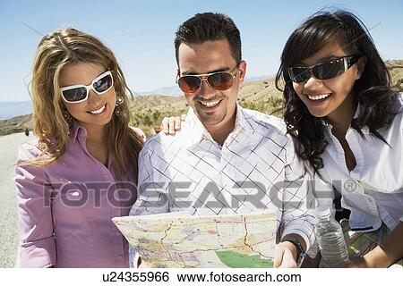 Stock Photograph - Three people looking at map on side of desert road. Fotosearch