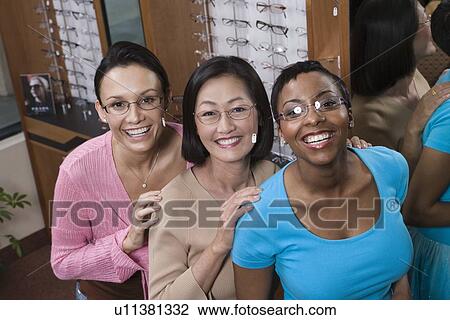 Stock Image - Three women wearing eyeglasses posing in store. Fotosearch