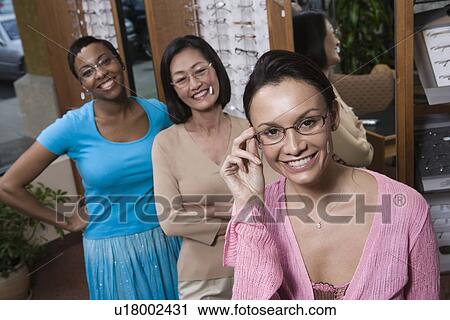 Stock Image - Three women wearing eyeglasses posing in store. Fotosearch