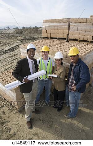 Two architects and two construction workers standing on construction site holding blueprints View Large Photo Image Stock Photo - Two architects and two construction workers standing on construction site holding blueprints. Fotosearch