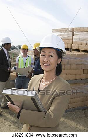 Picture - Two architects standing on construction site holding blueprints. Fotosearch