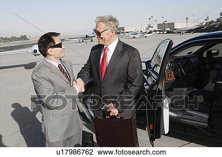 Two businessmen standing on landing strip in front of car and shaking hands. View Large Photo Image Stock Image - Two businessmen standing on landing strip in front of car and shaking hands.. Fotosearch