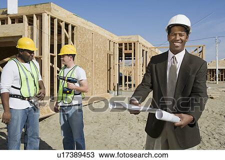 Stock Image - Two construction workers and surveyor holding blueprint. Fotosearch
