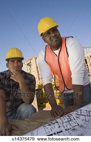 Stock Photo - Two construction workers leaning to table with blueprints. Fotosearch