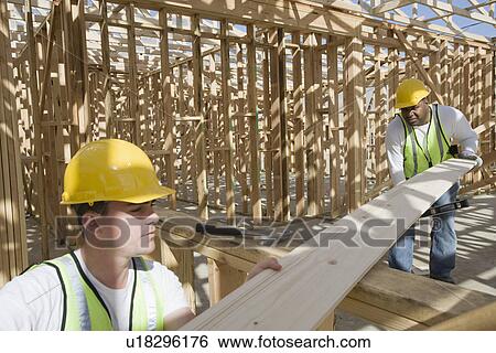 Stock Photograph - Two construction workers measuring wooden plank. Fotosearch