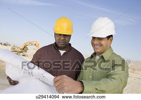 Picture - Two construction workers studying blueprint. Fotosearch