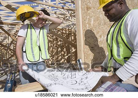 Stock Image - Two construction workers studying blueprints. Fotosearch