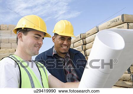 Stock Image - Two construction workers studying blueprints. Fotosearch