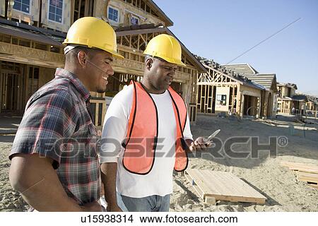 Picture - Two construction workers using mobile phone on construction site. Fotosearch
