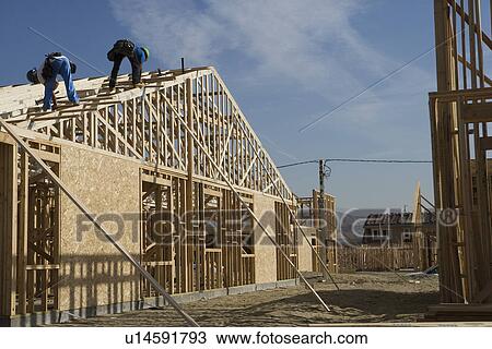 Stock Image - Two construction workers working on roof of half constructed house. Fotosearch