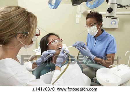 Stock Image - Two dentists examining female patient in surgery. Fotosearch