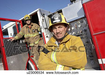 Two fire fighters standing by fire engine View Large Photo Image Picture - Two fire fighters standing by fire engine. Fotosearch