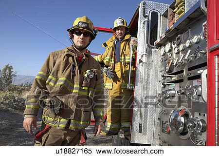 Stock Photography - Two fire fighters standing by fire engine. Fotosearch