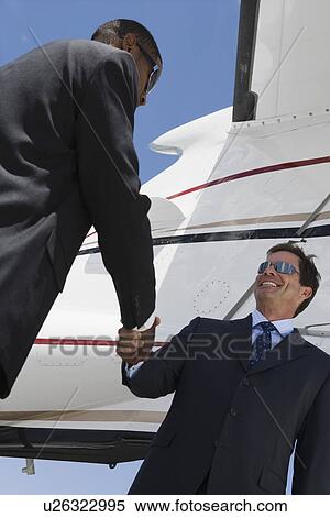 Two mid-adult businessman shaking hands in front of airplane, low angle view. View Large Photo Image Stock Photography - Two mid-adult businessman shaking hands in front of airplane, low angle view.. Fotosearch